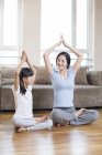 Young Chinese mother and daughter doing yoga at home — Stock Photo