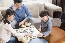Chinesische Kinder spielen Go, während der Vater auf dem Sofa zuschaut — Stockfoto