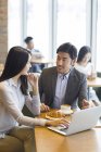 Chinese business people sitting and talking with laptop in cafe — Stock Photo