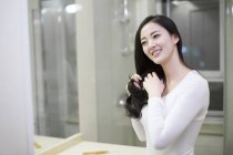 Chinese woman combing hair in bathroom — Stock Photo