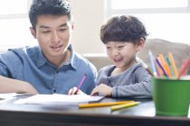 Chinese father helping cheerful son with homework — Stock Photo