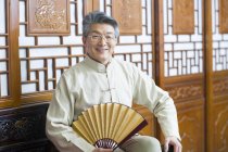Senior Chinese hält Vintage-Handheld-Ventilator im traditionellen Interieur — Stockfoto
