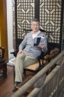 Senior Chinese man sitting in chair and reading journal — Stock Photo