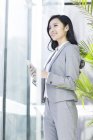 Китайський бізнес-леді проведення смартфон і фотографіях хтось дивитися вбік в офісі — стокове фото