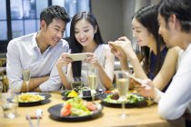 Китайские друзья фотографируют еду в ресторане — стоковое фото
