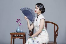 Китаянка в традиционном платье сидит за чайным столом и держит ручной вентилятор — стоковое фото