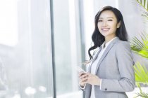 Chinesische Geschäftsfrau hält Smartphone in der Hand und blickt in die Kamera im Büro — Stockfoto