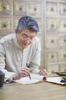 Chinesischer Arzt hält Heilkraut in der Hand und schreibt in Notizbuch — Stockfoto