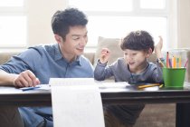 Padre e hijo chinos haciendo deberes juntos en la mesa - foto de stock