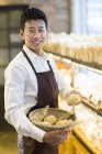 Китаец держит корзину со свежими булочками в пекарне — стоковое фото