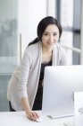 Китаянка, стоящая и пользующаяся компьютером в офисе — стоковое фото