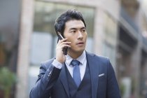 Китайский бизнесмен разговаривает по телефону, на городской сцене — стоковое фото