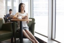 Mujer china sentada con smartphone y café en la cafetería - foto de stock