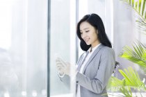 Empresaria china usando smartphone en edificio de oficinas - foto de stock