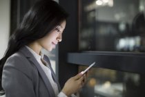 Femme d'affaires chinoise utilisant un smartphone par fenêtre de bureau — Photo de stock
