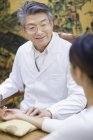 Senior Chinese doctor taking pulse of female patient — Stock Photo