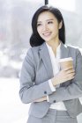 Chinese businesswoman holding cup of coffee at work — Stock Photo