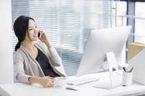 Chinese woman talking on phone at workplace — Stock Photo