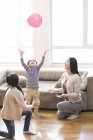 Chinese mother and children playing with balloon at home — Stock Photo