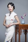Китаянка в традиционной одежде опирается на стол с орхидеями — стоковое фото