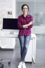 Chinese woman leaning on table with arms folded in office — Stock Photo