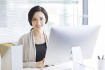 Chinese woman sitting at desk in office and looking in camera — Stock Photo