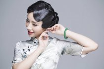 Chinese woman in traditional dress putting on earrings — Stock Photo