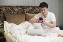 Uomo cinese utilizzando smartphone a letto — Foto stock