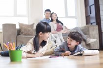 Chinois frères et sœurs étudier ensemble au sol avec des parents sur canapé regarder — Photo de stock