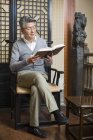 Senior uomo cinese seduto sulla sedia e lettura del libro — Foto stock