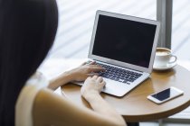 Жінка працює з ноутбуком в кафе, вид ззаду — стокове фото