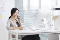 Китайська жінка, що говорити по телефону на робочому місці — стокове фото