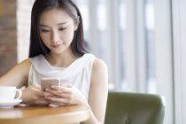 Chinese woman using smartphone in coffee shop — Stock Photo