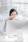 Chinese businesswoman using headset at workplace — Stock Photo