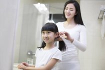 Mãe chinesa pentear cabelo filha no banheiro — Fotografia de Stock