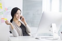 Chinese woman talking on phone at workplace — Stock Photo