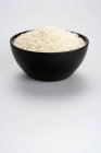Неварений рис в чорній мисці ізольований на білому тлі — стокове фото