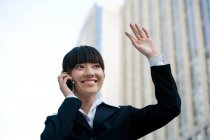 Donna cinese che parla al cellulare, sorride e agita la mano — Foto stock
