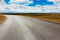 Road with distant mountains view and cloudy sky, Tibet, China — Stock Photo