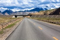 Bridge on road with mountains view and cloudy sky, Qinghai Province — Stock Photo