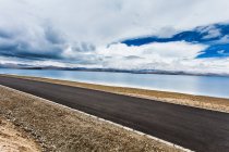 Road with lake and mountains view and cloudy sky, Tibet, China — Stock Photo