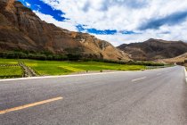 Carretera con vistas a las montañas y cielo nublado, Tíbet, China - foto de stock