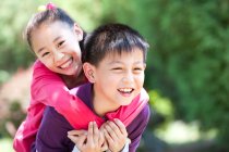 Portrait of young Chinese boy giving girl piggyback ride — Stock Photo