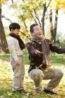 Китайский мальчик с дедушкой смотрит, как падают листья — стоковое фото