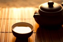 Taza de té y olla en la estera de bambú, tiro de cerca - foto de stock