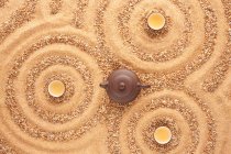 Blick auf Teekanne und Tassen auf Sandoberfläche — Stockfoto