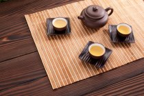 Conjunto de té de cerámica china con olla y tazas llenas en estera de bambú - foto de stock