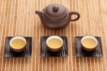 Conjunto de té de cerámica china con olla y tazas llenas en estera de bambú - foto de stock
