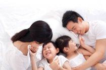 Счастливая китайская семья лежит в постели — стоковое фото