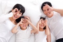 Feliz familia china acostada en la cama - foto de stock